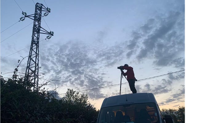 Silhouette of a man with an infrared camera standing on a van, with the camera pointed at a power cable.