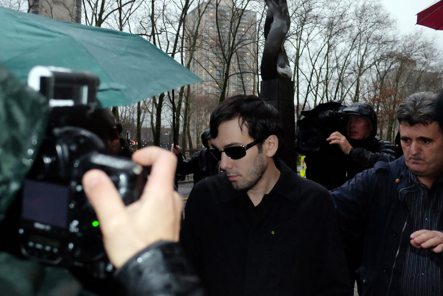 Martin Shkreli walks through a swarm of journalists as he leaves the courthouse after his arraignment. His father is standing just behind him.