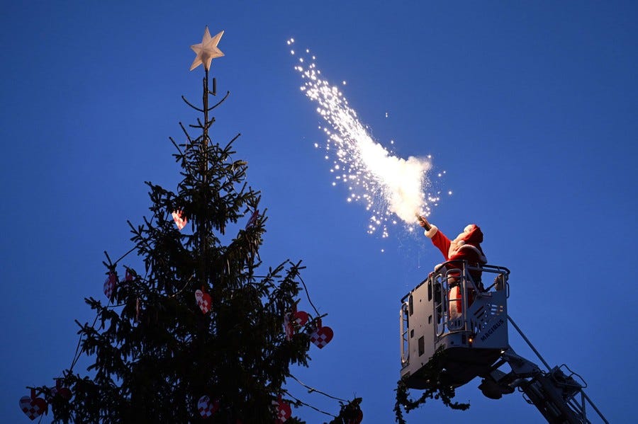 A man dressed as Santa Claus stands in the bucket of a lift and uses a bright flare to light a Christmas tree.
