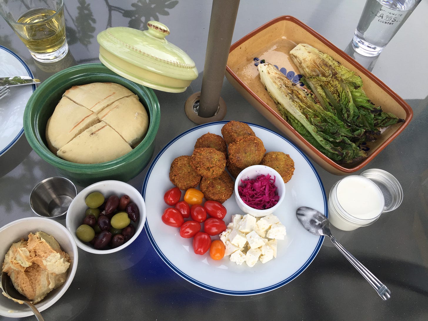 a set of serving dishes and plates with mezze items on an outdoor table. See caption for list of items.
