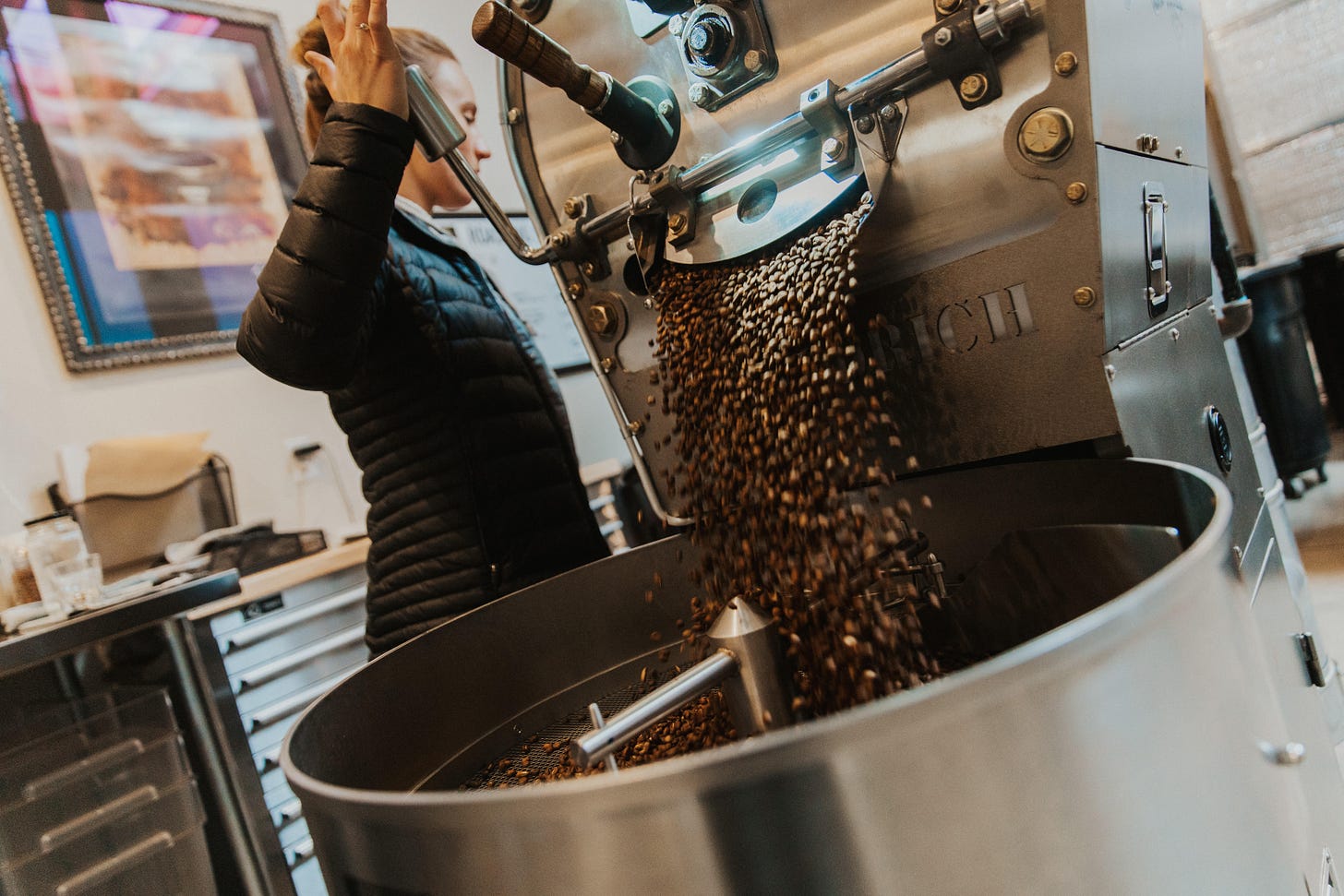 Breanna Briggs, head roaster of Leap Coffee shifting a release lever and opening a hatch on a coffee roaster allowing the coffee beans to flow out into a stainless steel barrel.