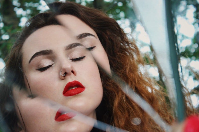 A person with long hair, a nose ring and red lipstick reflected in a shattered mirror. A person with long hair, a nose ring and red lipstick reflected in a shattered mirror.