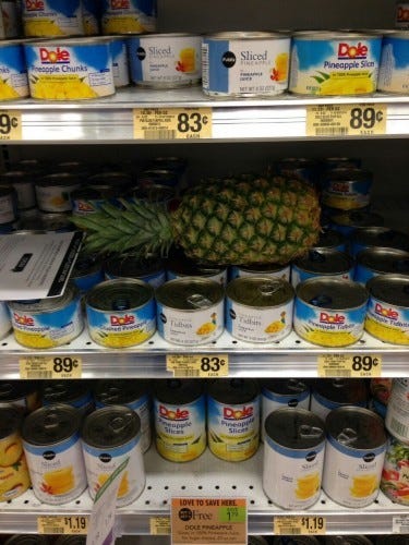 Whole pineapple left on supermarket shelf with tinned pineapple chunks