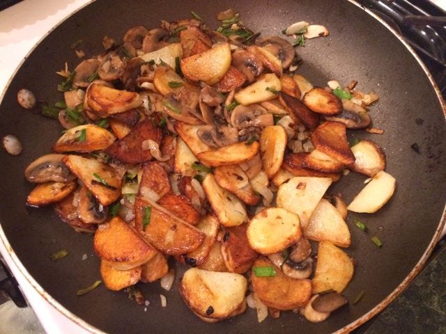 A pan with browned potato pieces and mushrooms in it
