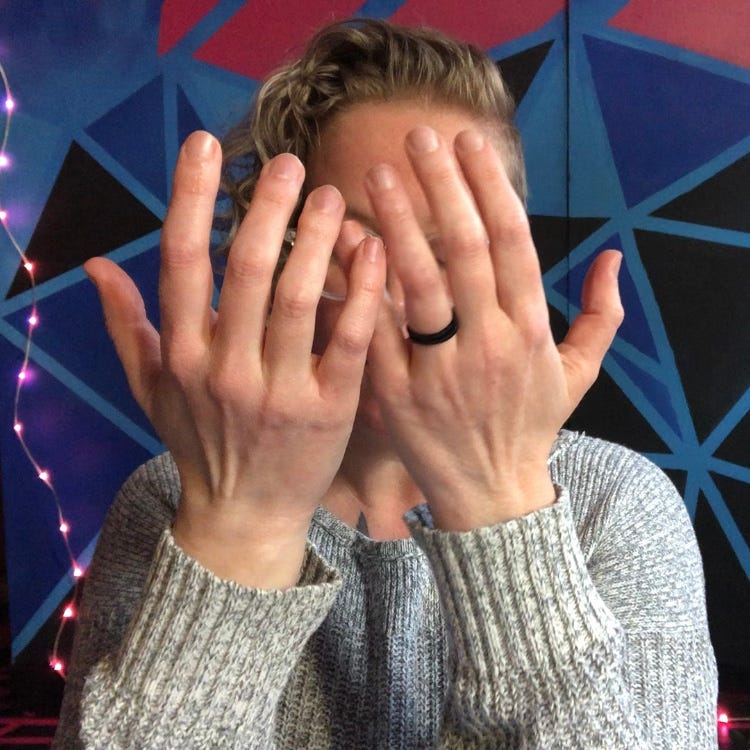 a person in front of a geometric background with hands held up obscuring their face
