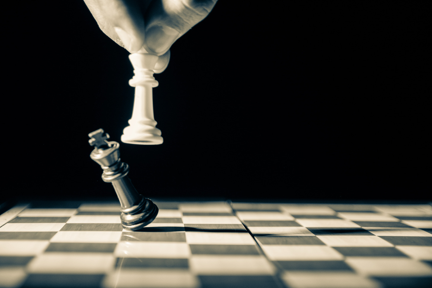 Black and white photo of a chess piece knocking over another chess piece on a chess board.(GR Stocks / Unsplash)