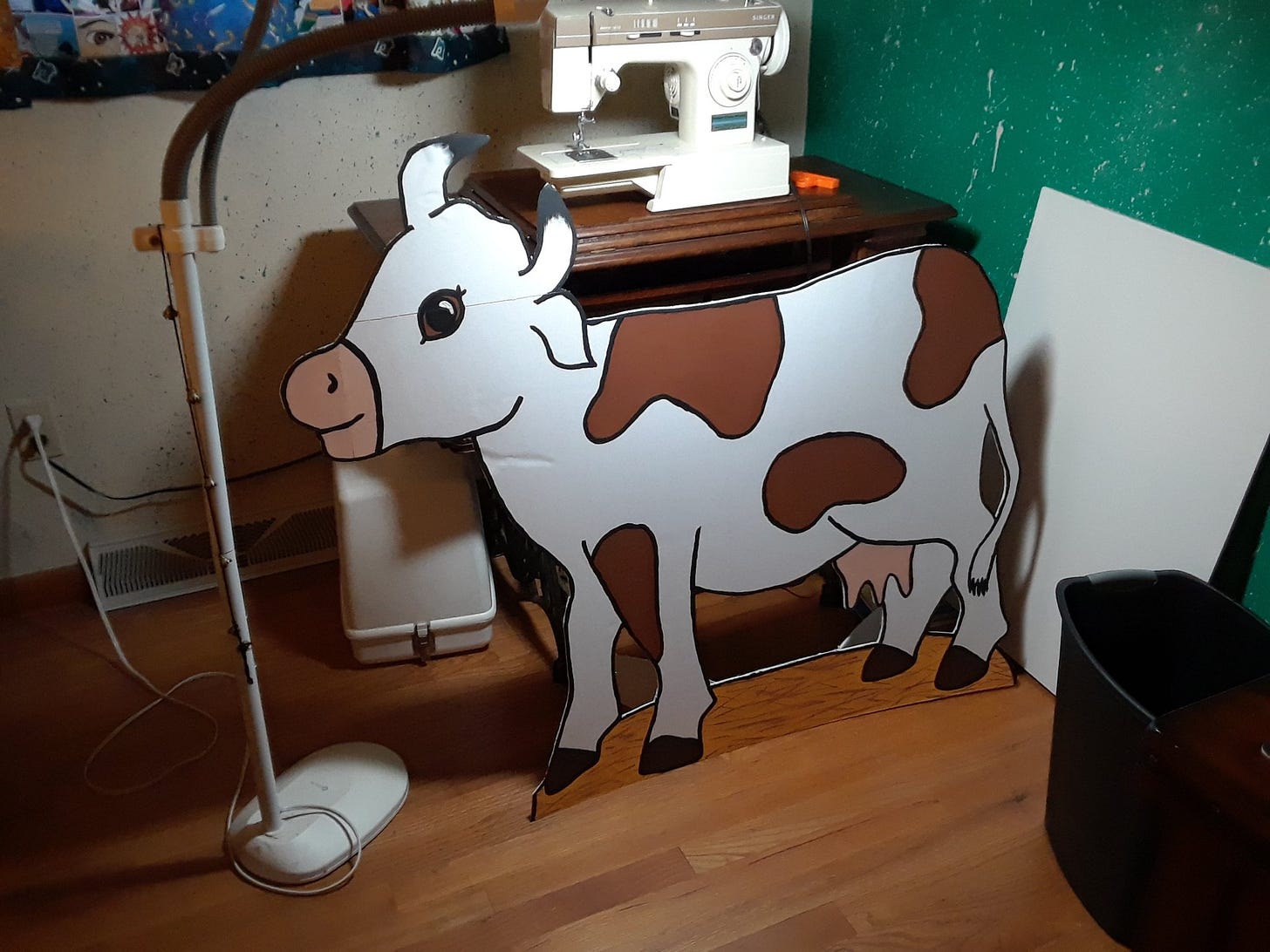 A brown and white foamboard cow stands in front of a sewing table.