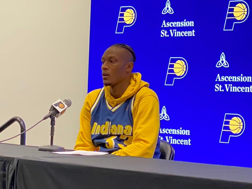 Myles Turner wears a retro Pacers jersey while at the podium after a game.