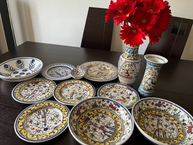 Hand-painted ceramic plates, typical of the Coimbra style, arrayed on a black table with red flowers. 