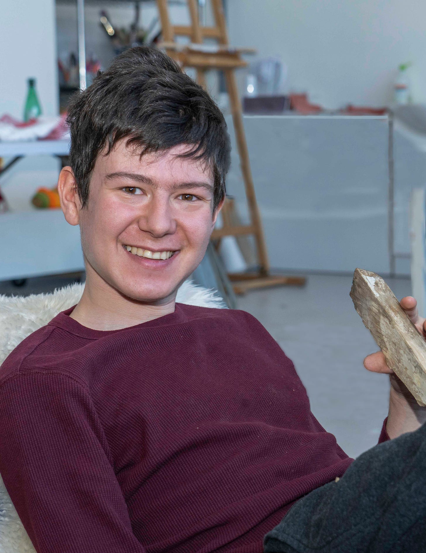 A headshot of Adam Wolfond. He has short brown hair and is wearing a maroon shirt. He is sitting and smiling. Photo credit: Michael Klar.