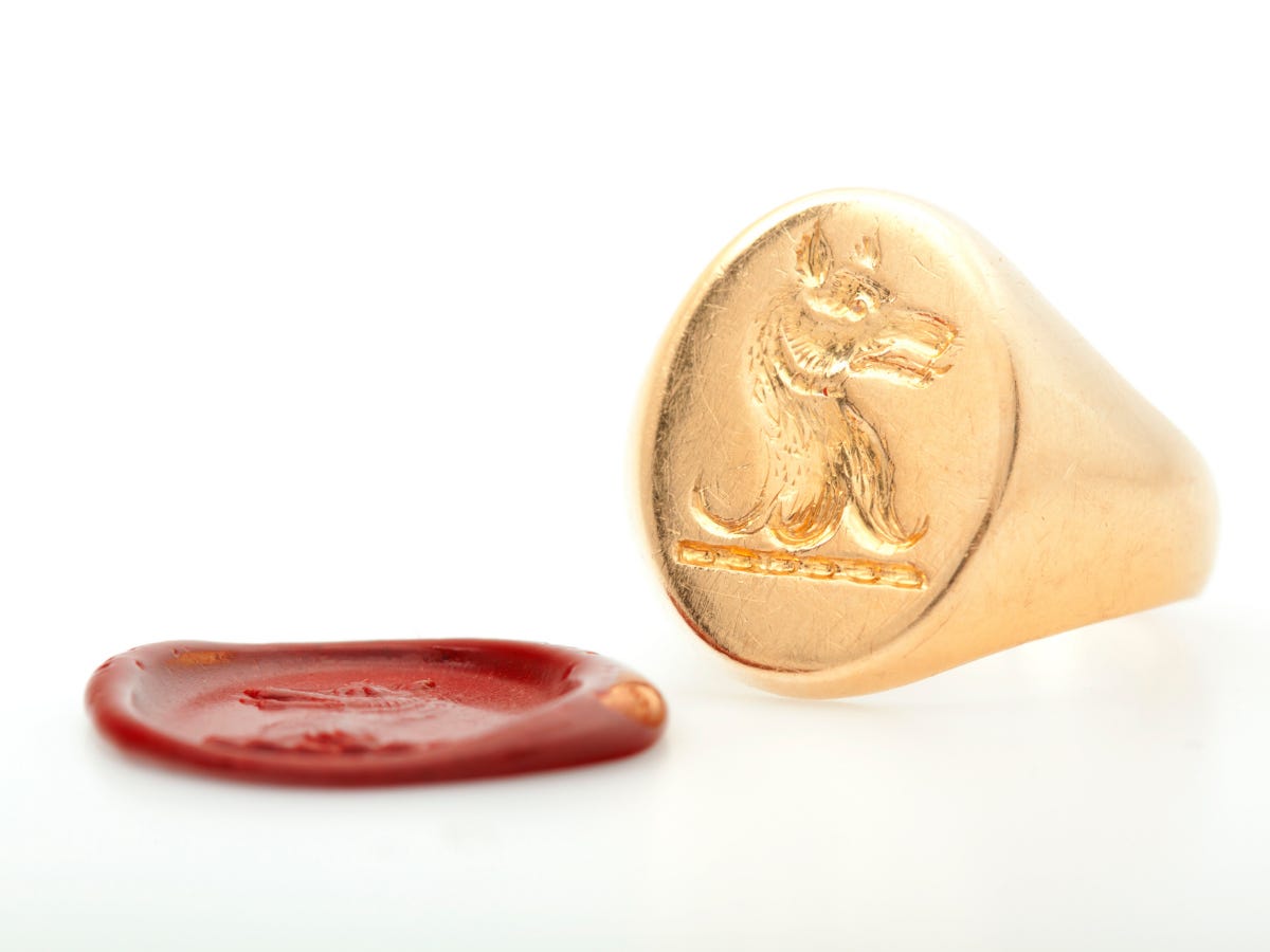A gold signet ring rests near a red wax real