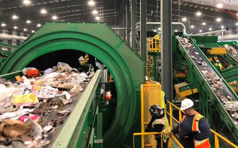 the interior of a large building with a lot of conveyor belts, including a closeup of one with garbage and a man with a hardhat on a ladder 