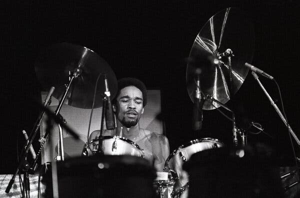 Fred White, a light-skinned Black man with a goatee, behind a large drum kit with an intense look on his face.