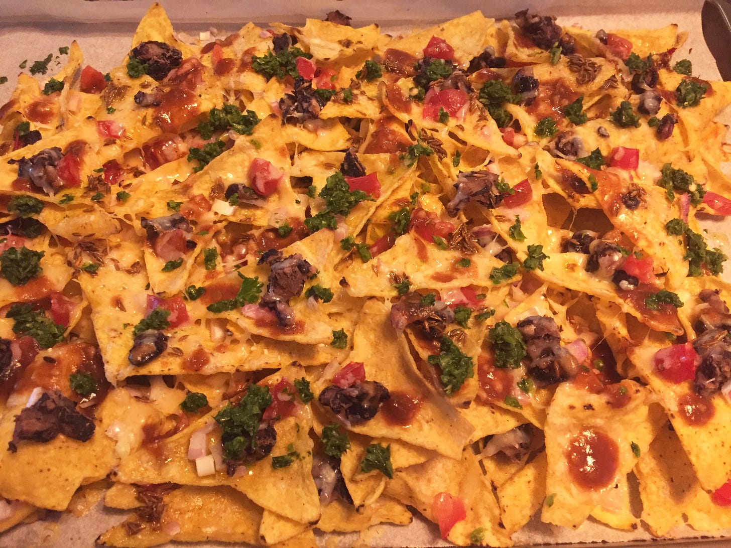 Nachos made with yellow corn tortilla chips, white cheddar, black beans, red onion, tomato, and cilantro chutney and tamarind sauce drizzled overtop.