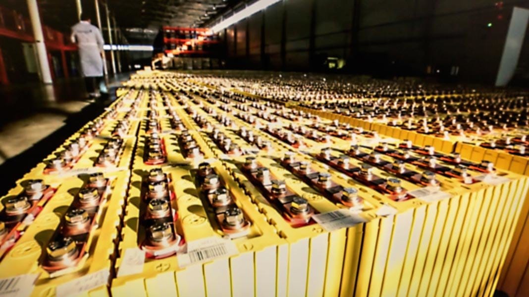 A lot of batteries lined up in a factory. A man is walking away from the camera in the background