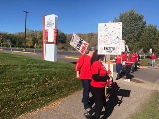 picketers with red shirts stand on the sidewalk holding signs