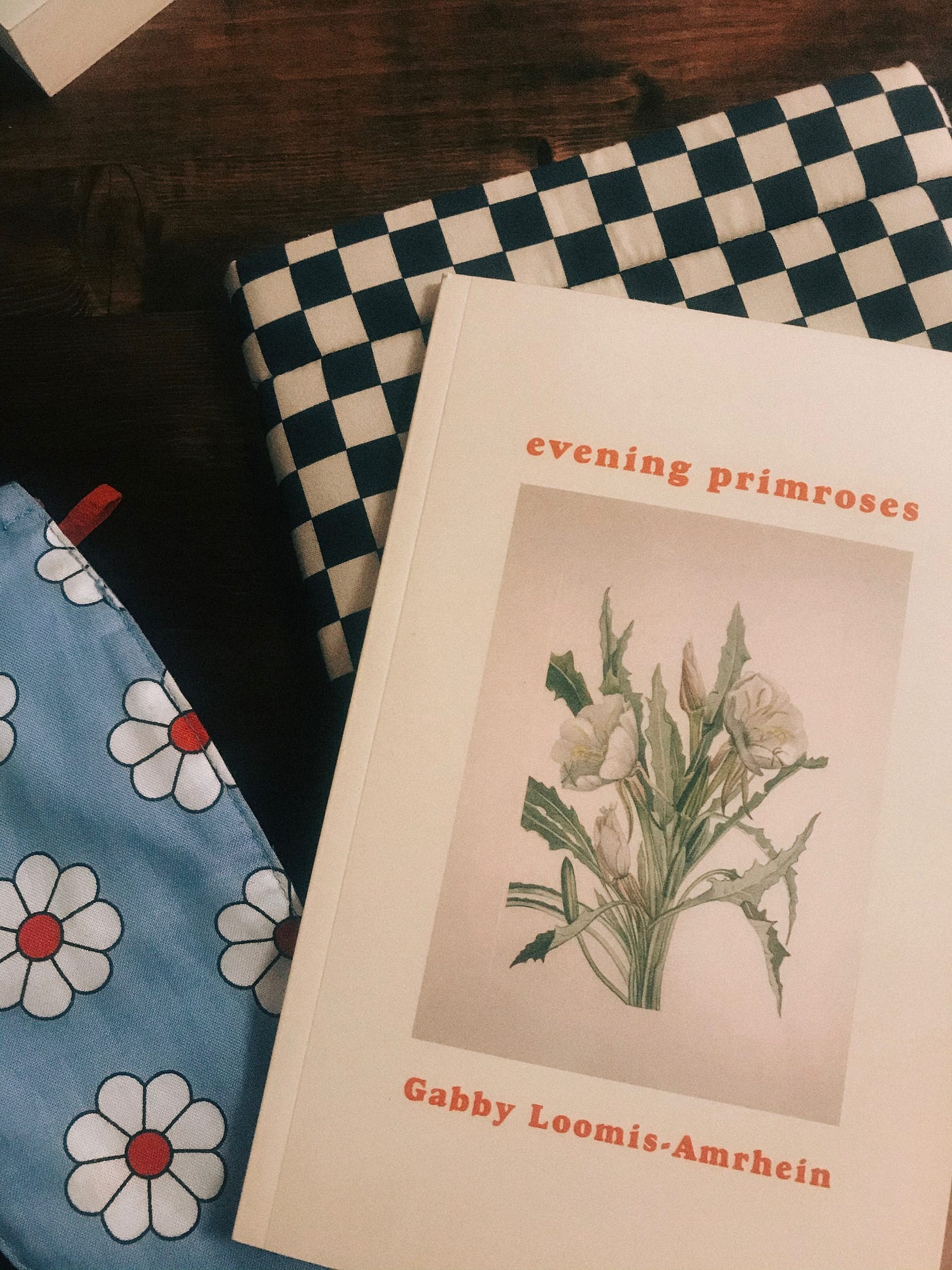 evening primroses sits on top of a black & white checkered book sleeve. Next to the sleeve is a blue face mask with white flowers.