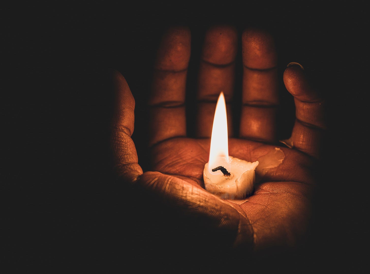 A burning candle sits in the palm of an open hand