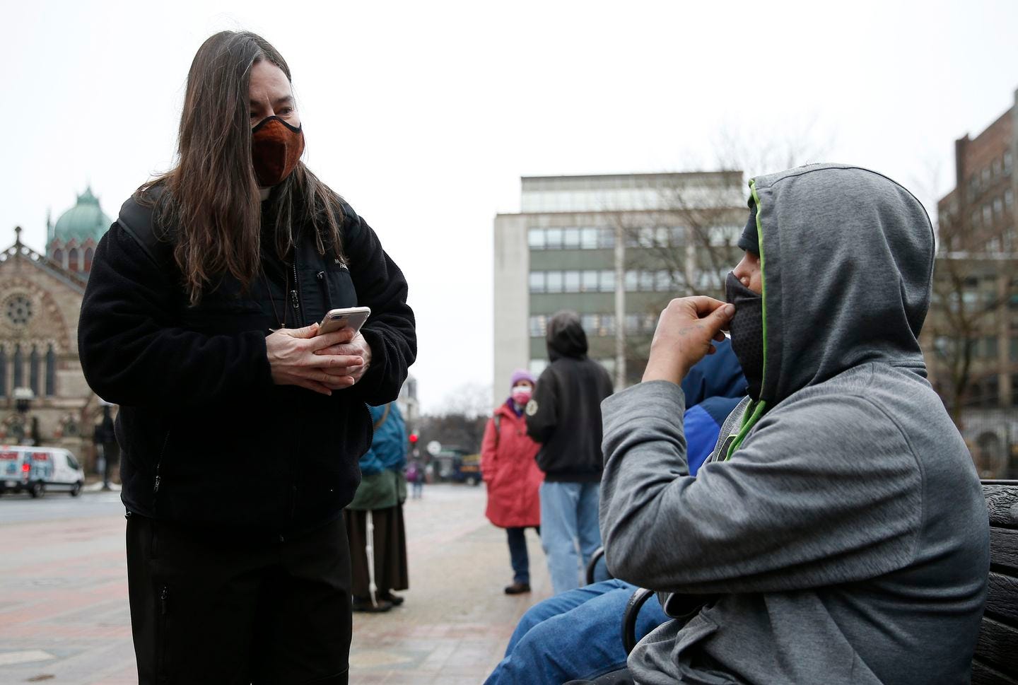 Boston, MA -- 3/1/21 -- Lisa Loughlin, a chaplain who is part of 'Common Cathedral' an organization which has ecumenical services on Boston Common, offers her phone to a homeless man in Copley Square who had asked to use it so he could try and call a family member.  (Jessica Rinaldi/Globe Staff)