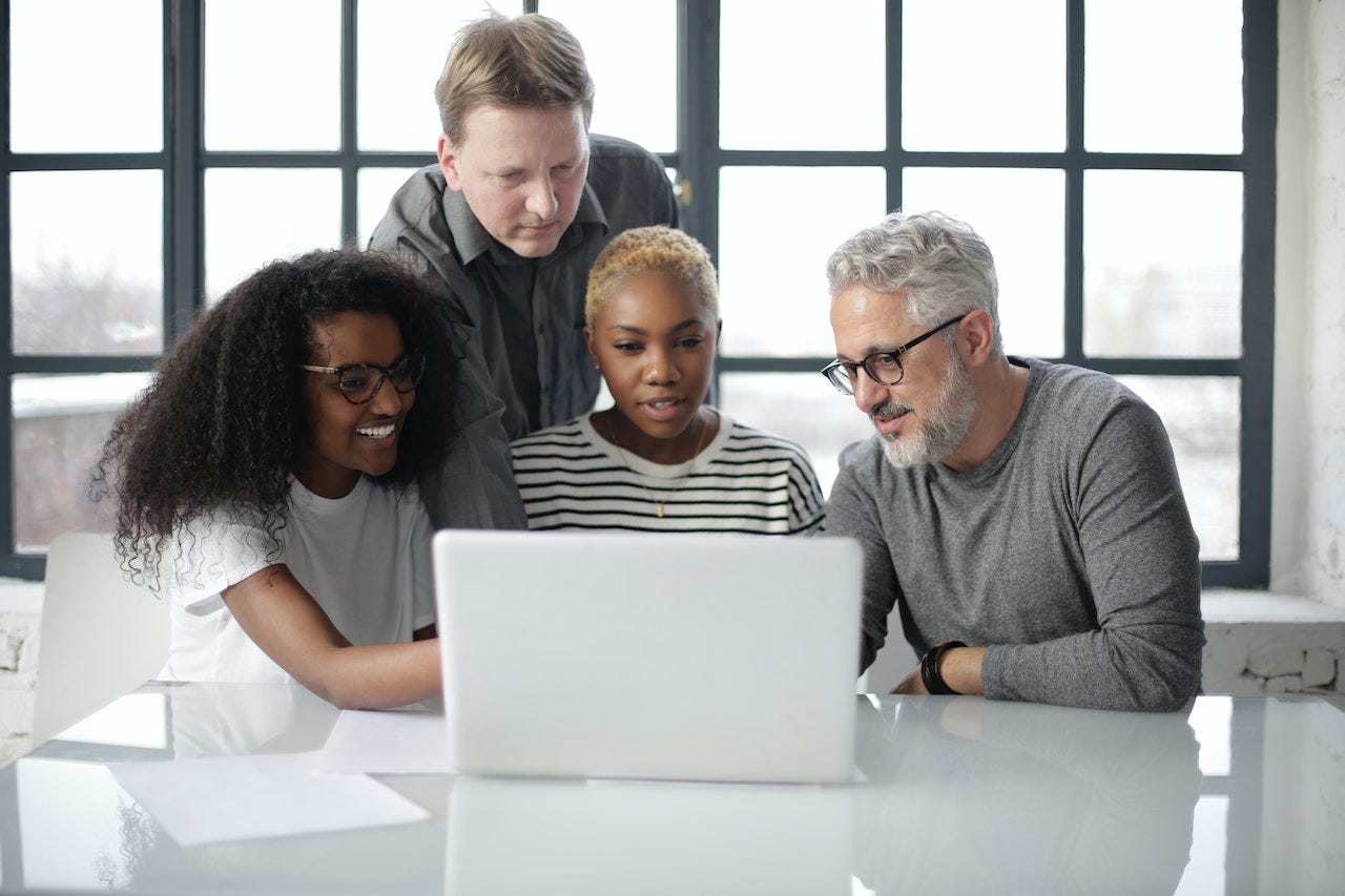 2 black women and 2 white men looking at something on the computer screen. 4 generations: Gen Z, Millennial, Gen X, and Baby Boomer