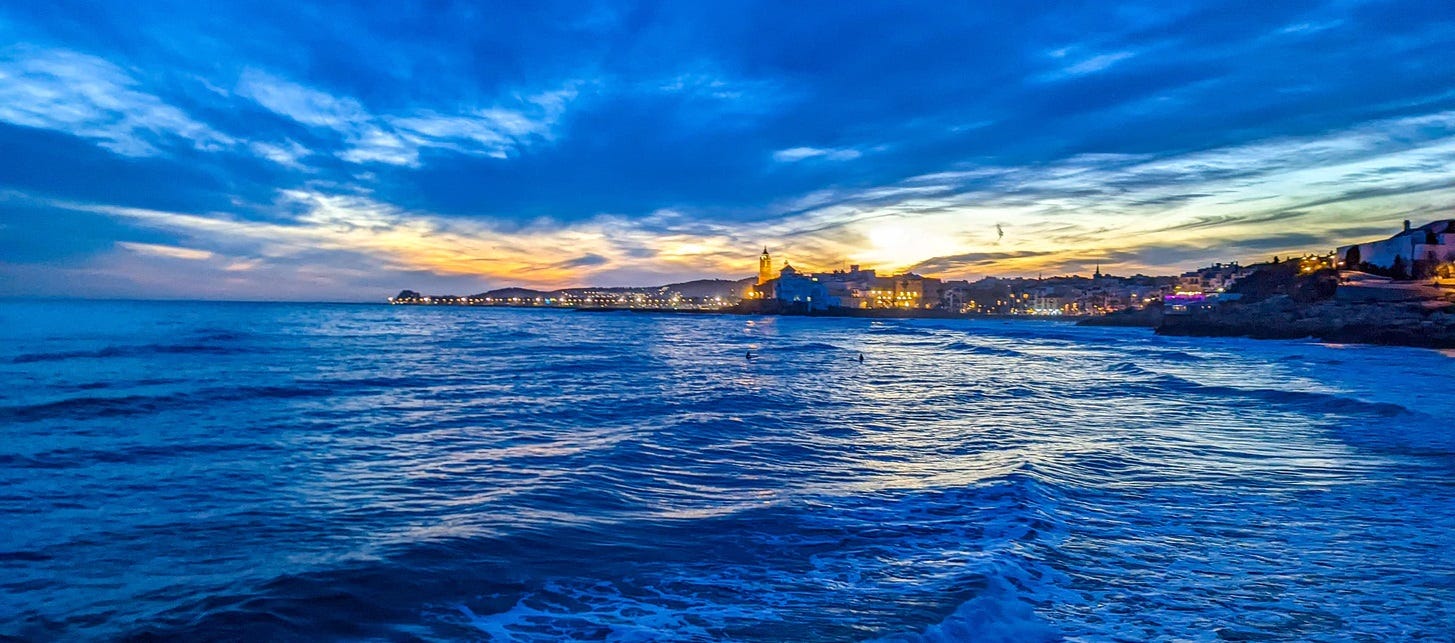A picture of Sitges taken from farther up the coast beneath an overcast sky casting blue colors over everything. 