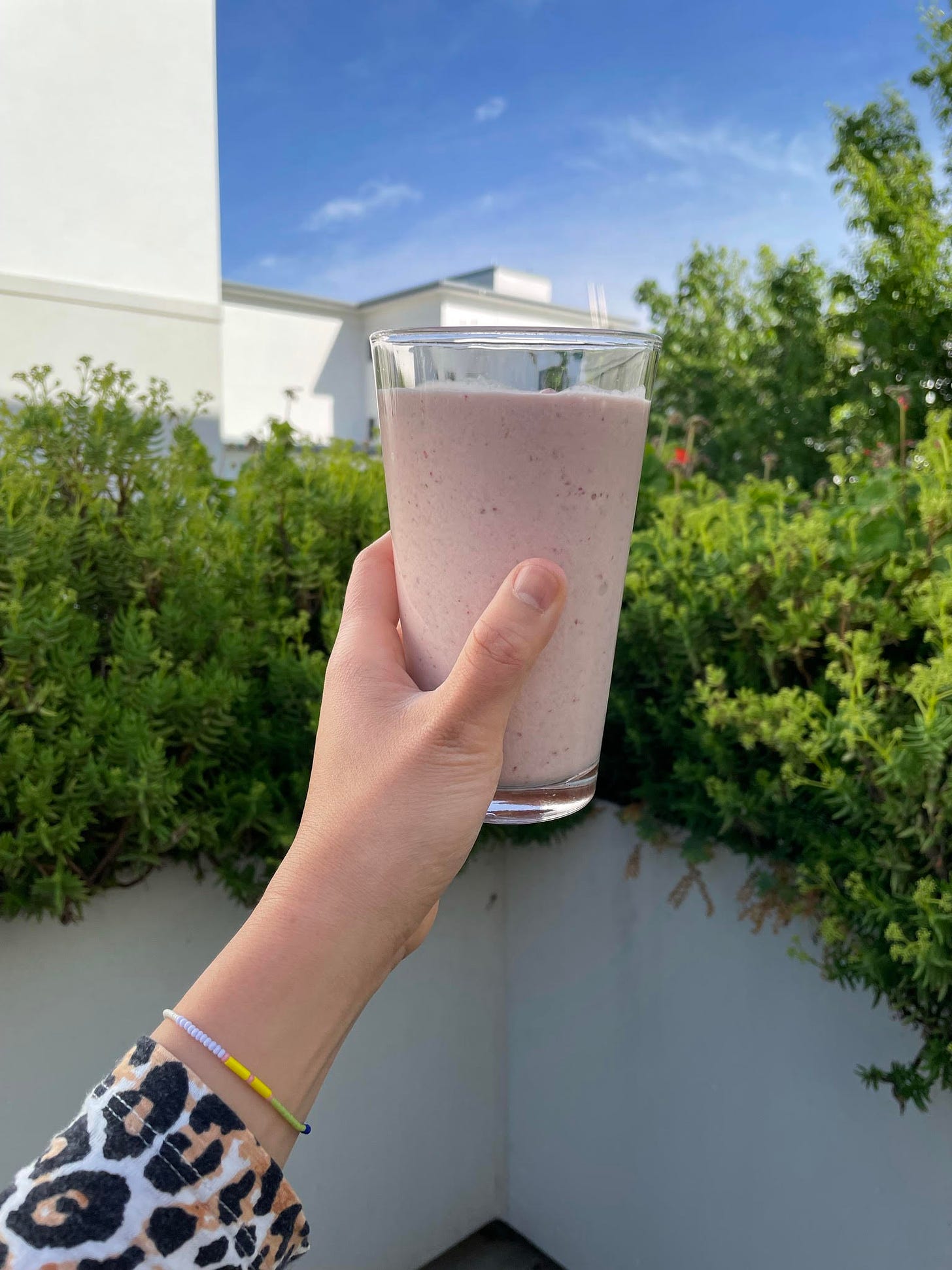 A strawberry smoothie held against the backdrop of flower boxes on a sunny balcony.
