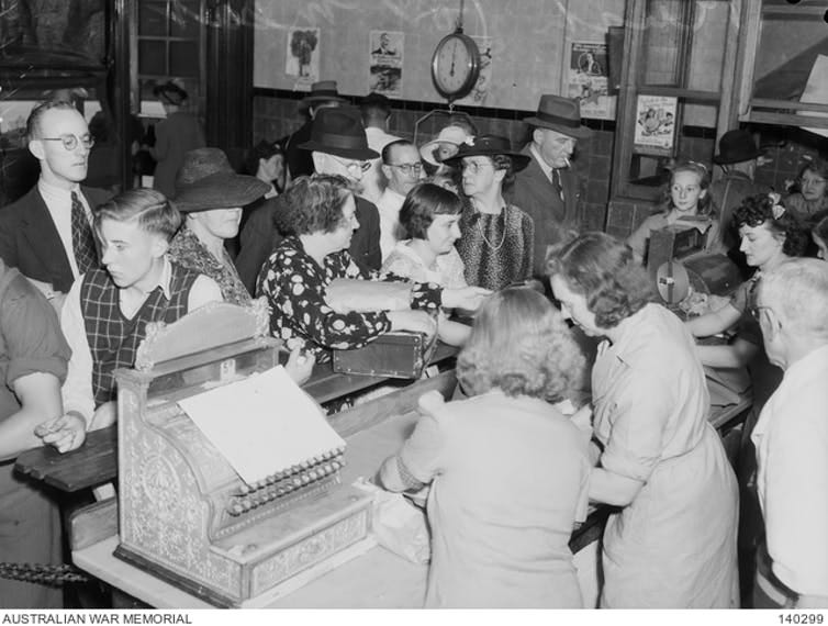 Black and white photo, people crowd a small shop.