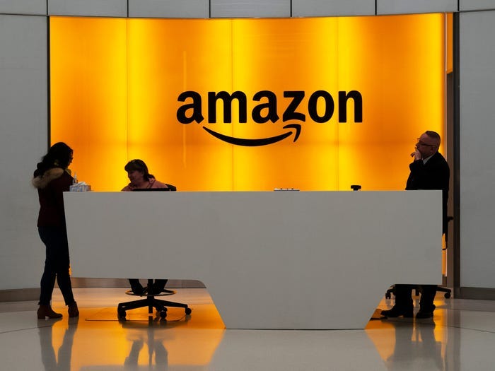 Amazon office front-desk staff stand in front of an orange sign with the Amazon smile logo