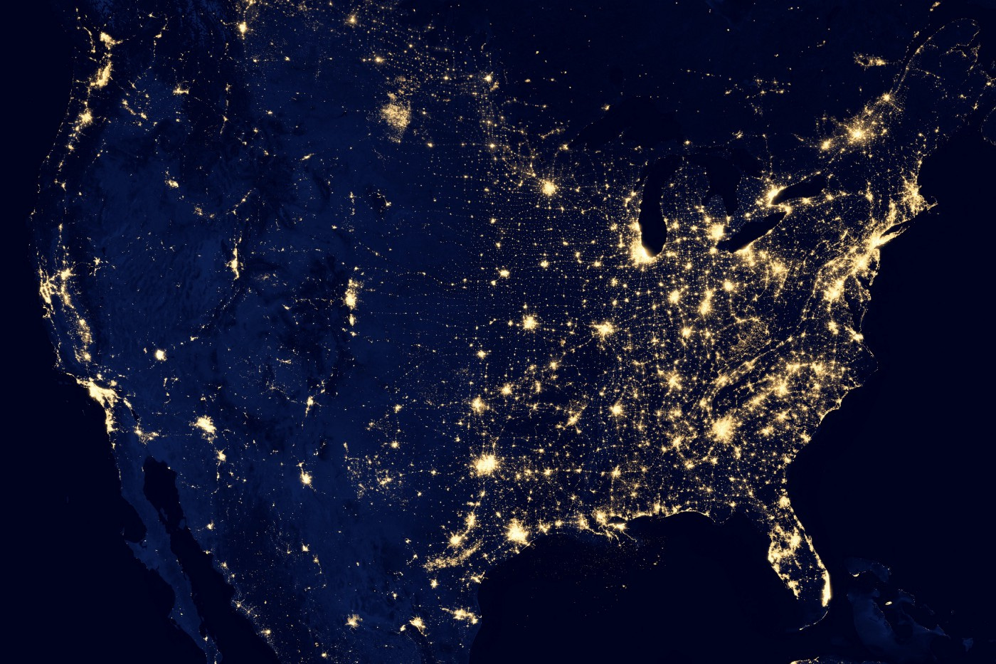 A map of the US at night from space. The east side is filled with lights while the west side is less lit up with the exception of the West coast.