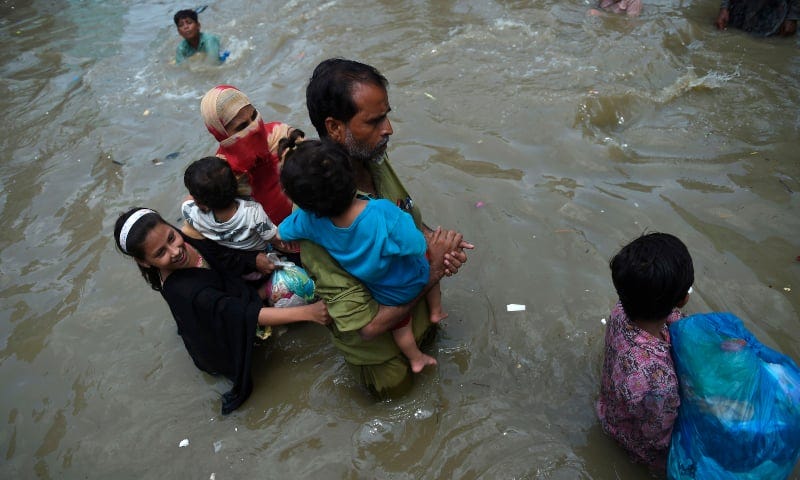A family wades through a flooded street after heavy monsoon rains in Karachi on August 22. — AFP