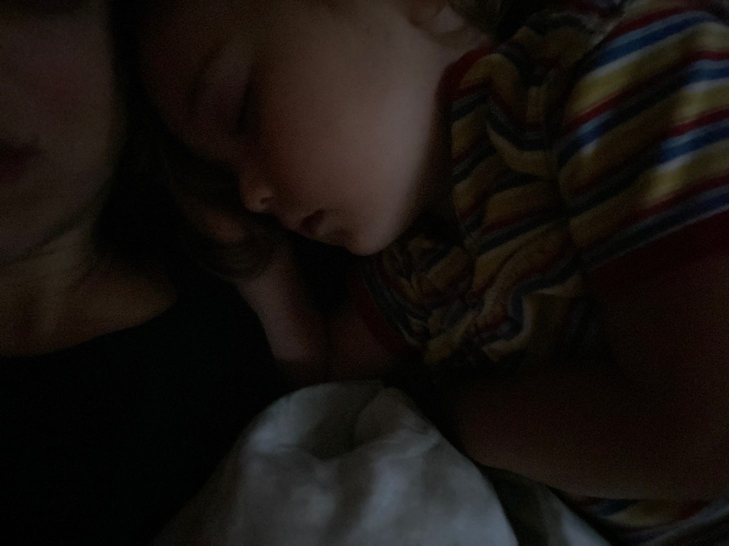 A blurry portrait of a sleeping toddler lying on the chest of their mom, whose face is only partially in the frame.