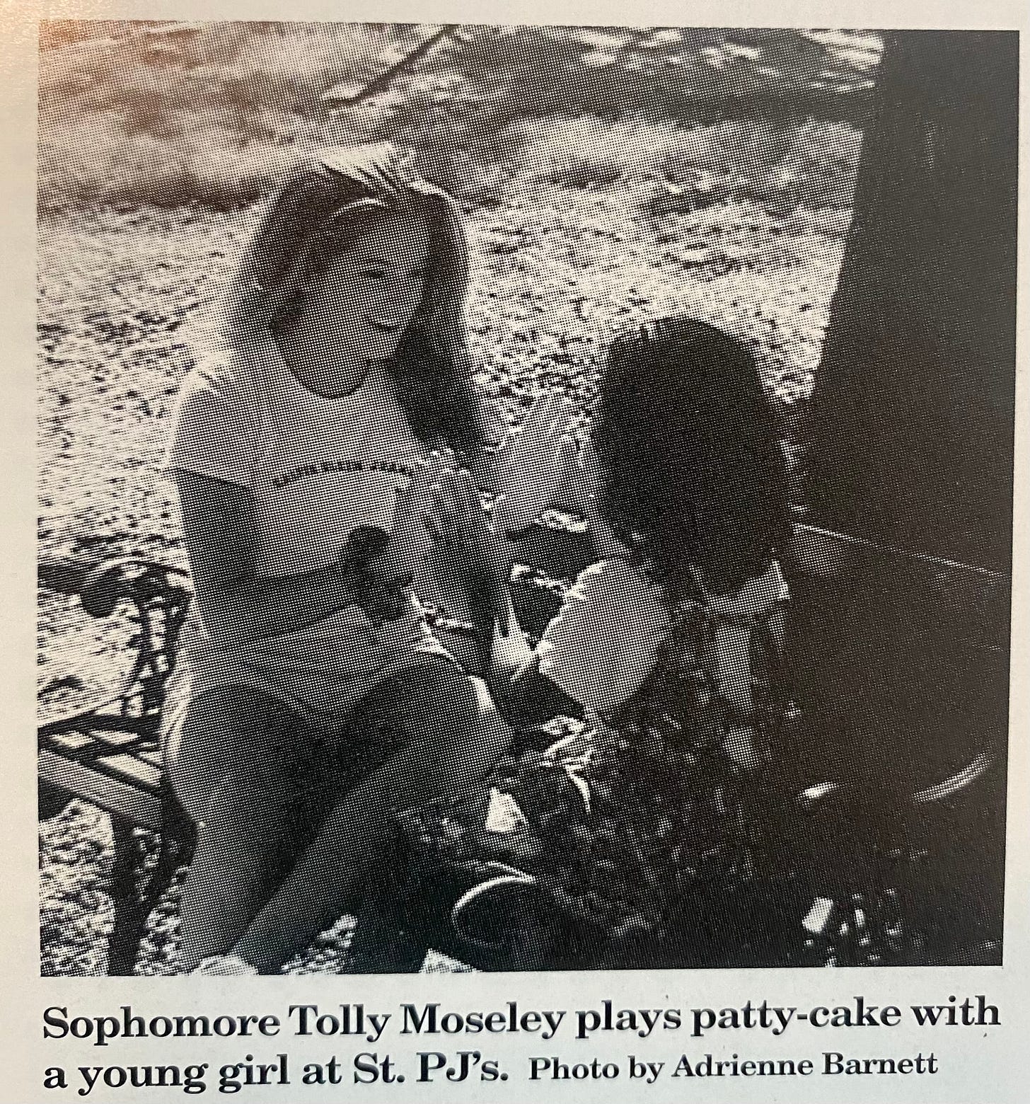 A young Tolly in shorts and a t-shirt plays pattcake with a little curly-haired girl in an old newspaper clipping.