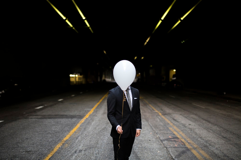 man in formal suit standing while holding white balloon