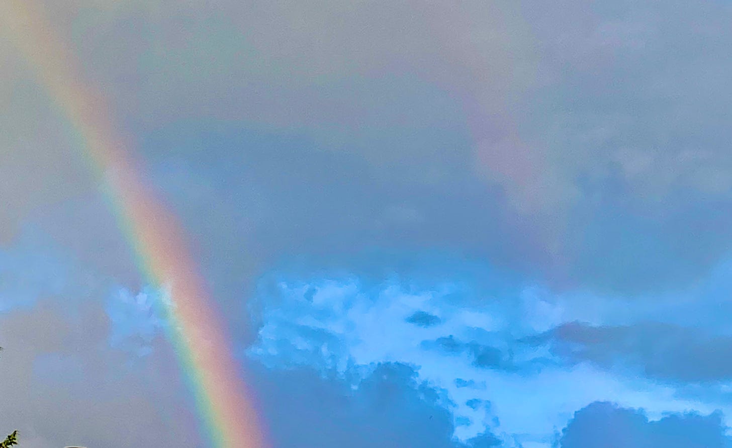 Double rainbows against cloudy sky.