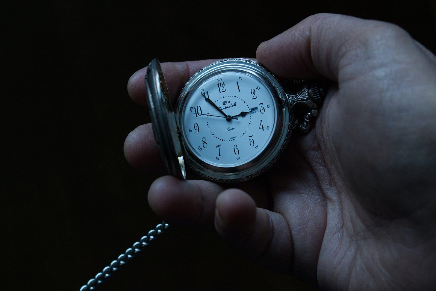 person holding pocketwatch with time visible