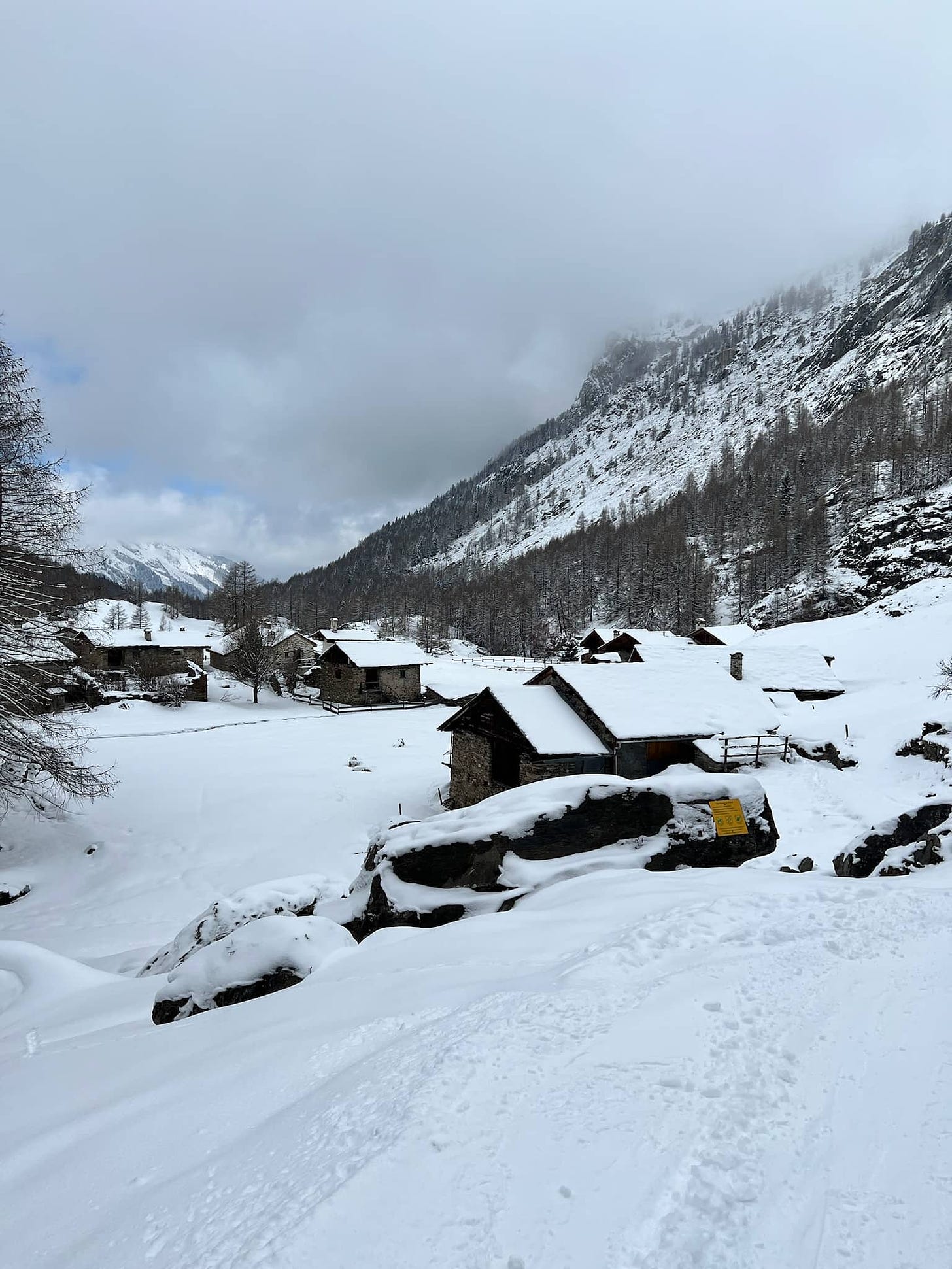 A photo of the village, Le Monal. It has a handful of small shack-like buildings covered in snow.