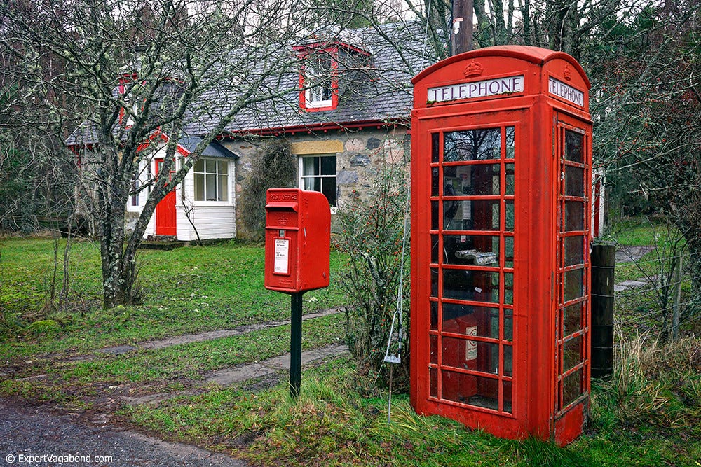 A british red telephone box, next to a letter box, in what seems to be a very rural setting