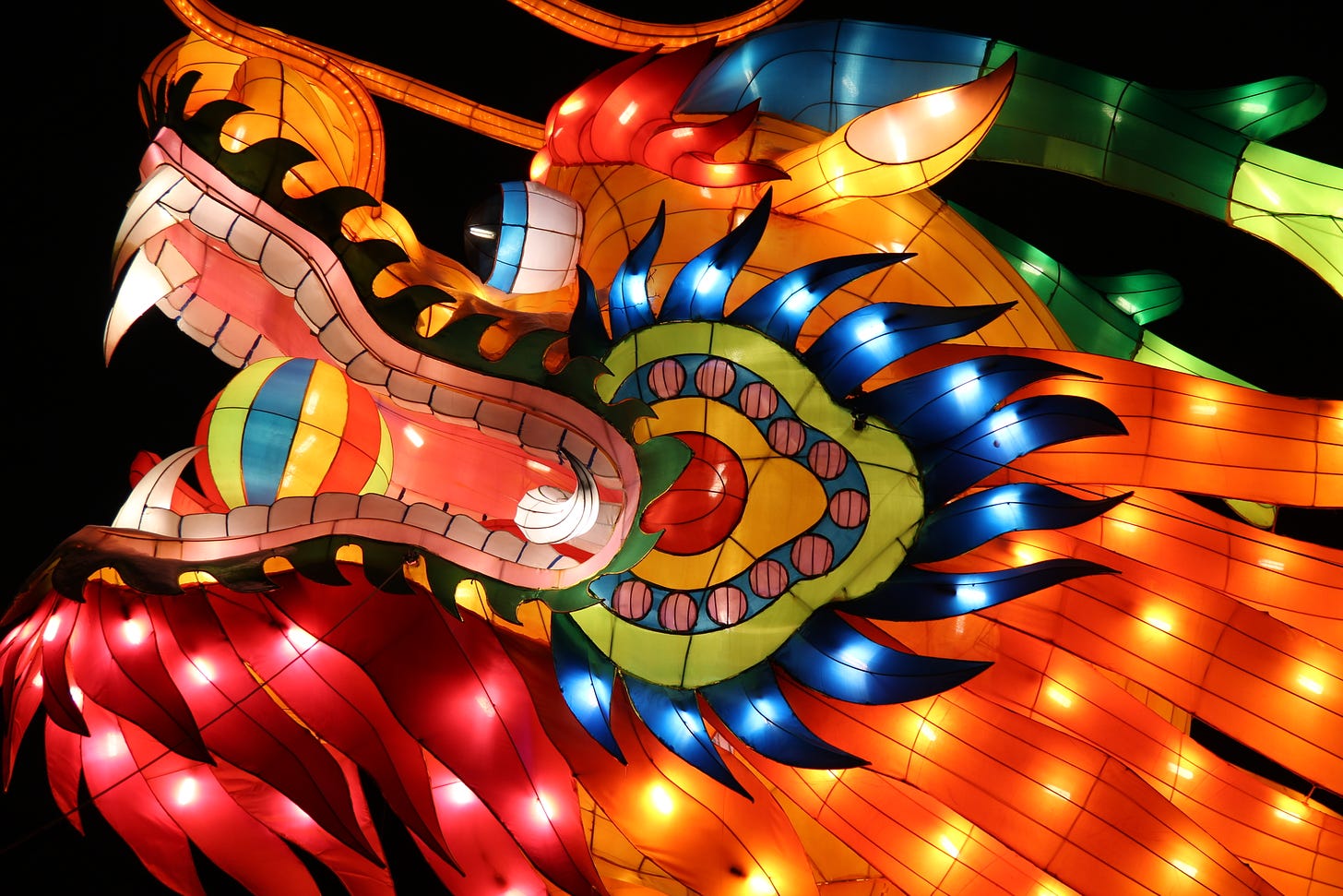 A dragon in a variety of vibrant colors as red and orange and decorated with lights against a black background.