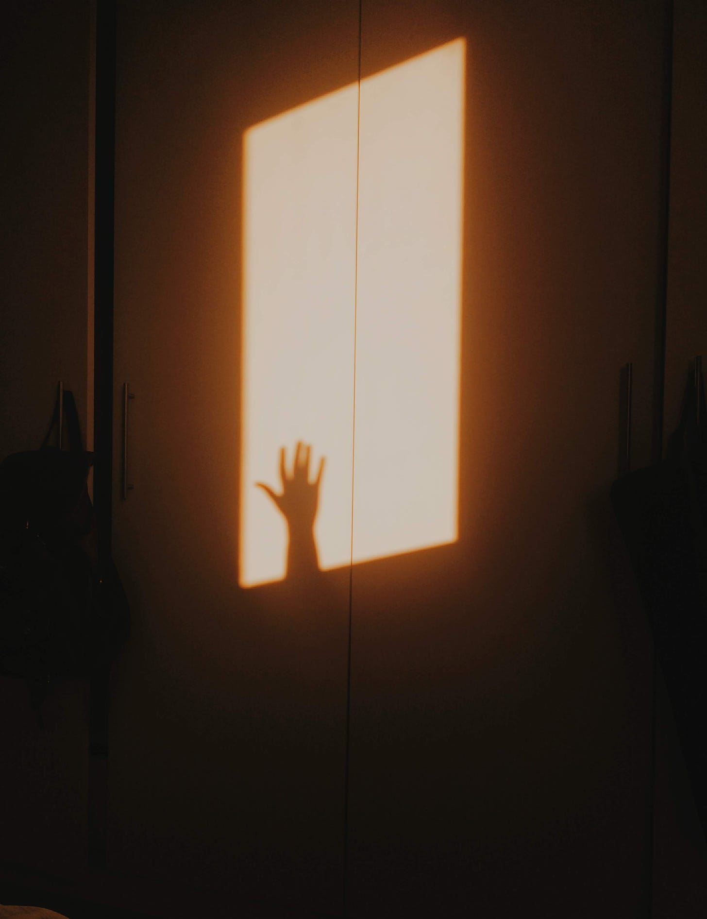 Foto da sombra de uma mão na porta do armário. A luz que ilumina a cena é a do amanhecer, deixando todo o ambiente amarelado.