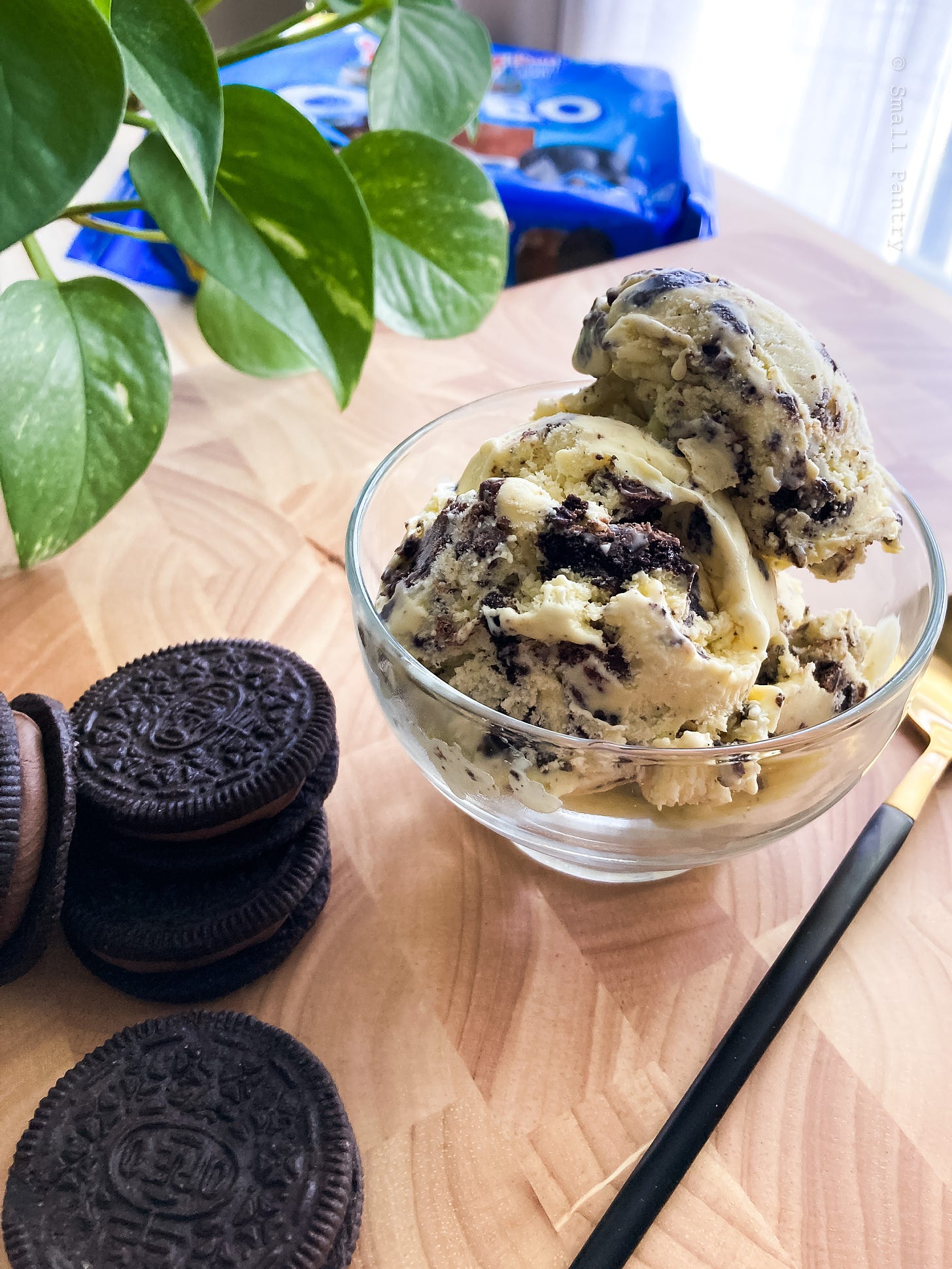 Small bowl of ice cream next to a pile of cookies, with a blue oreo package in the background.