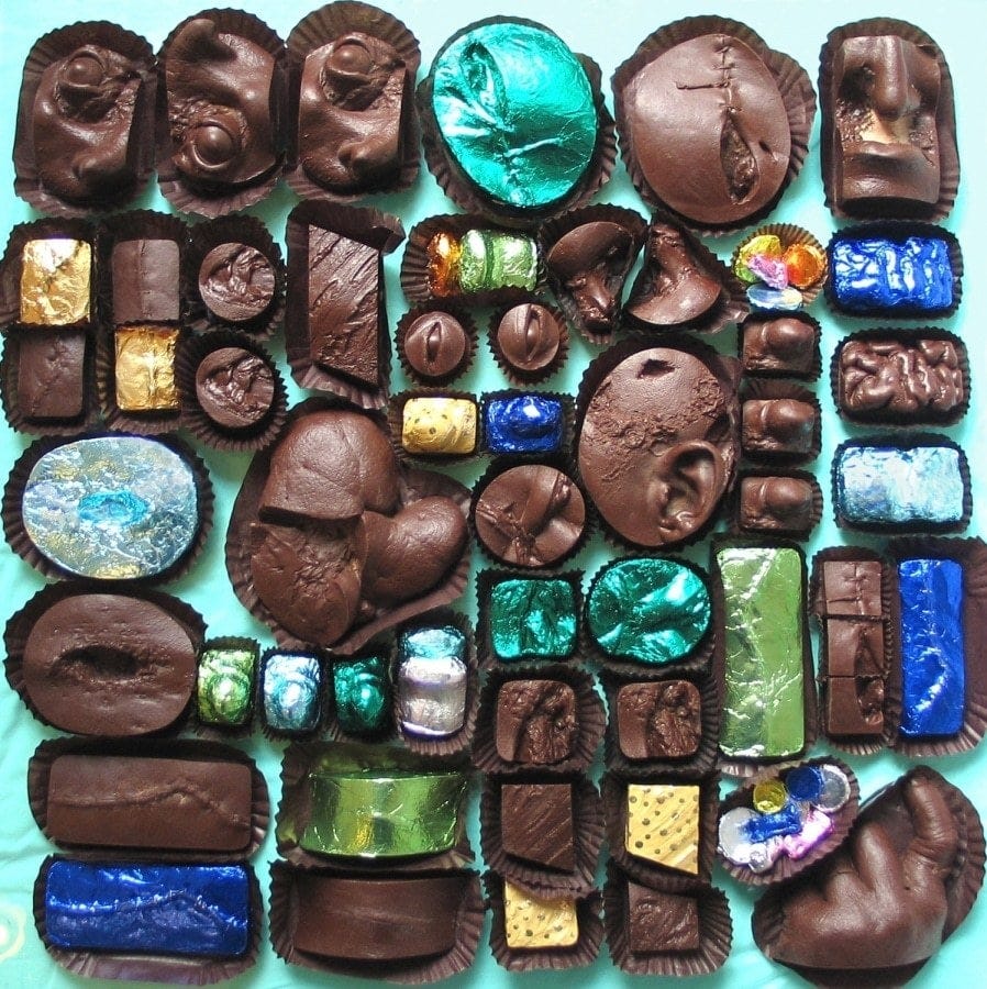 An assortment of dozens of chocolates in little paper cups on a robin’s egg blue surface. At first they just seem oddly shaped and lumpy, and it’s difficult to tell what you’re seeing. But then some details start to jump out: an ear, an eye. Then you can see the ones with sutures partway undone, one that looks like it might be part of an organ. Some resist interpretation even once you understand what you’re looking at. Whatever the Venn diagram intersection of “festive” and “disturbing” is, you’re looking at it.