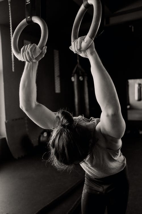 Grayscale Photo of a Person Holding Gymnastic Rings