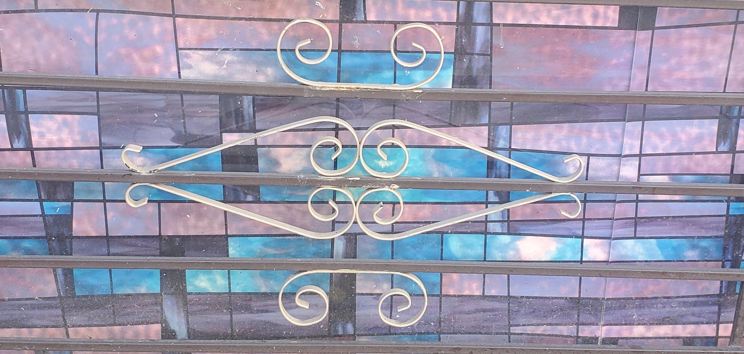 Beige pieces of metal in shapes reminiscent of a heart are placed in front of a purple and blue stained glass window.