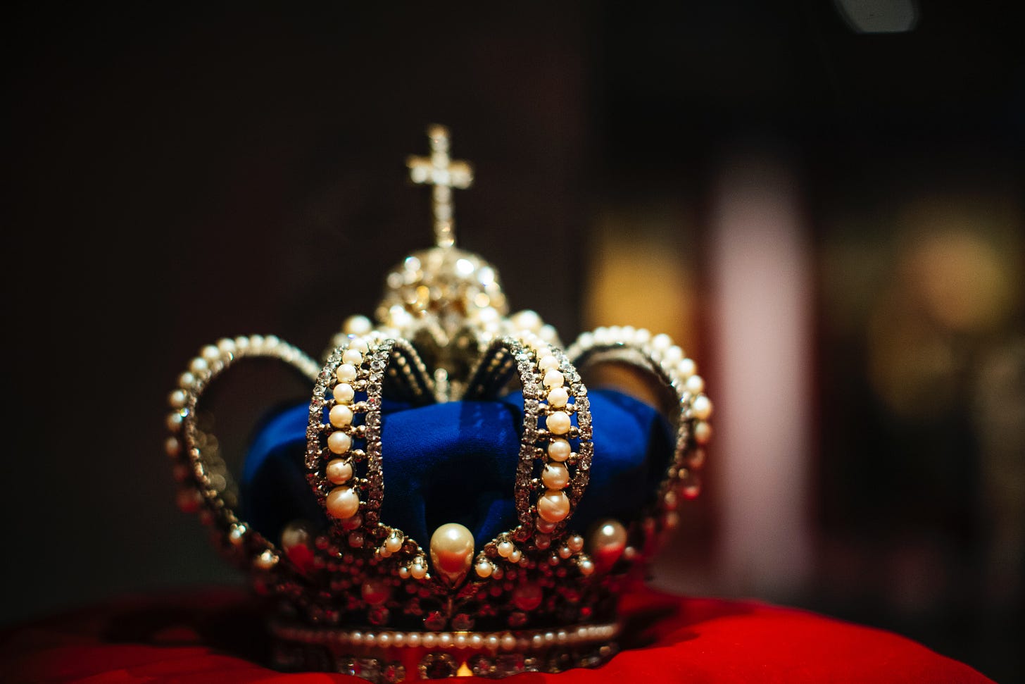 A gold crown with blue sits on a red velvet pillow