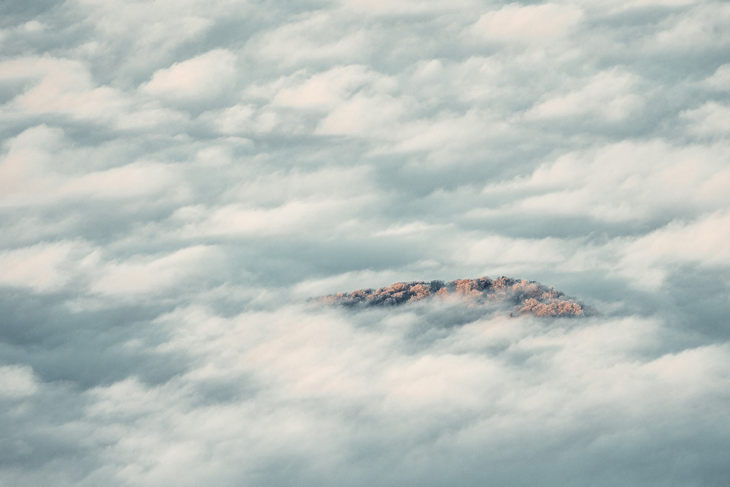 Mountain peak emerging through thick layer of clouds