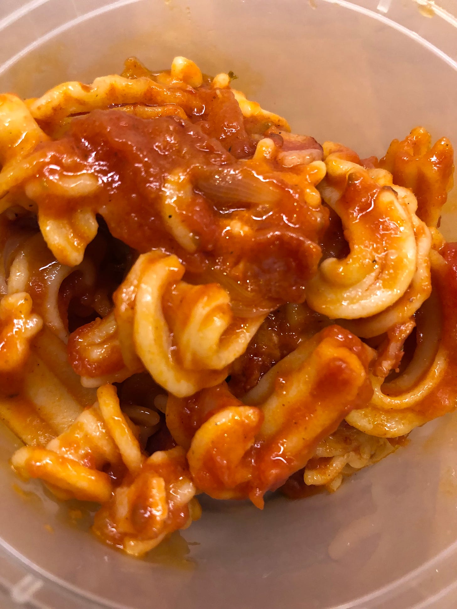 A container full of cascatelli noodles coated in tomato sauce