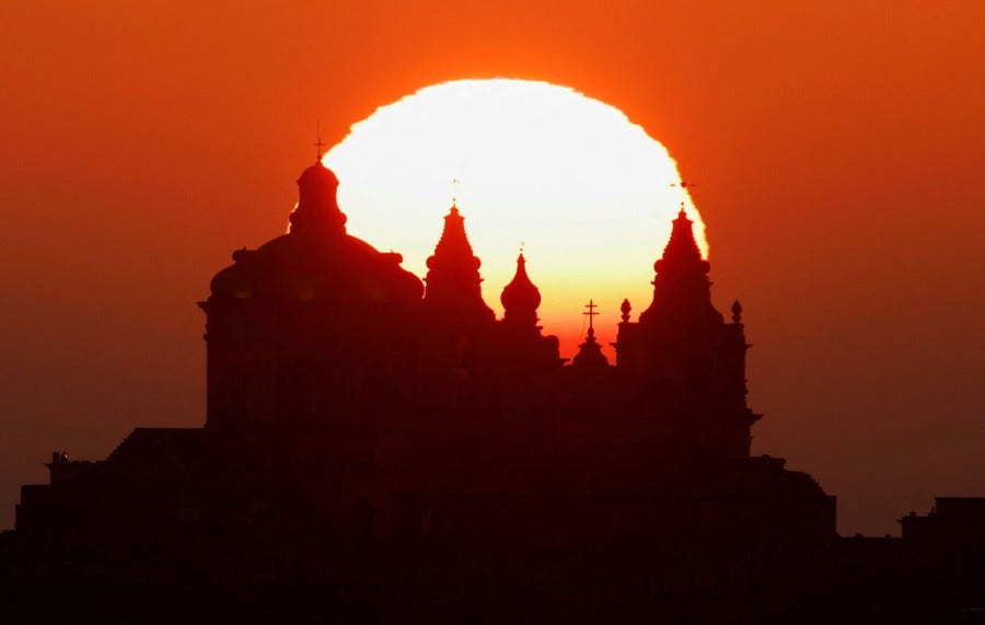 The sun rises behind a cathedral.