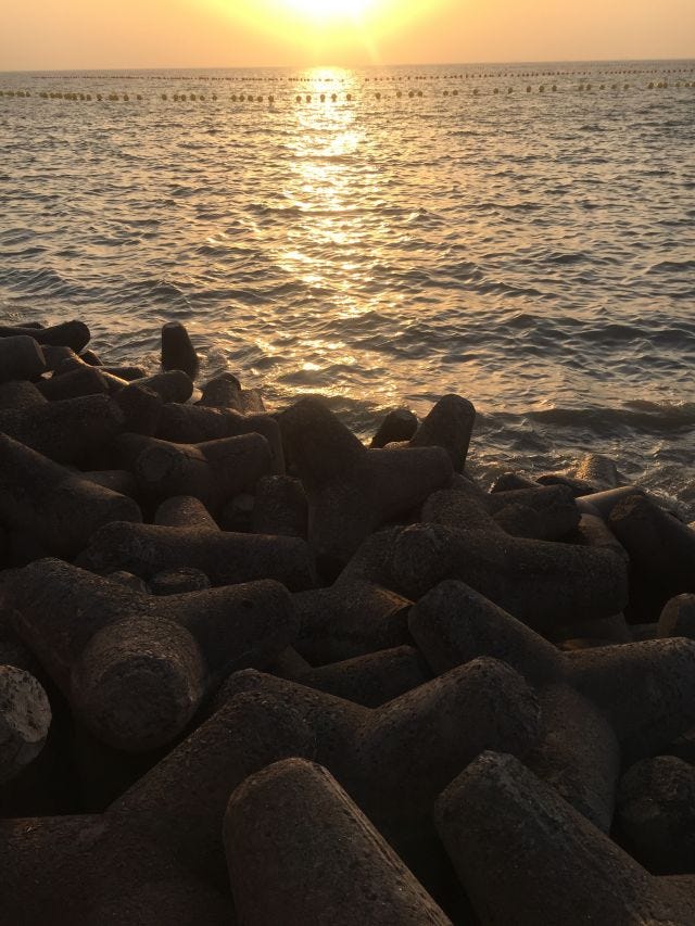A photo of a sun setting with rocks before the ocean.