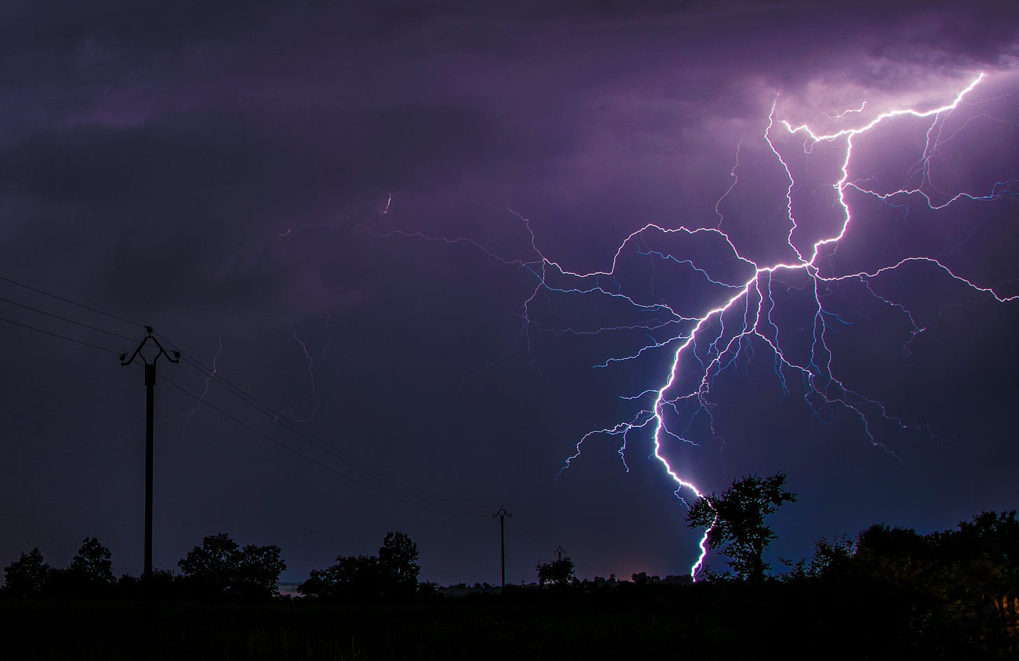 A purple bolt of lightning strikes the ground against a night sky.