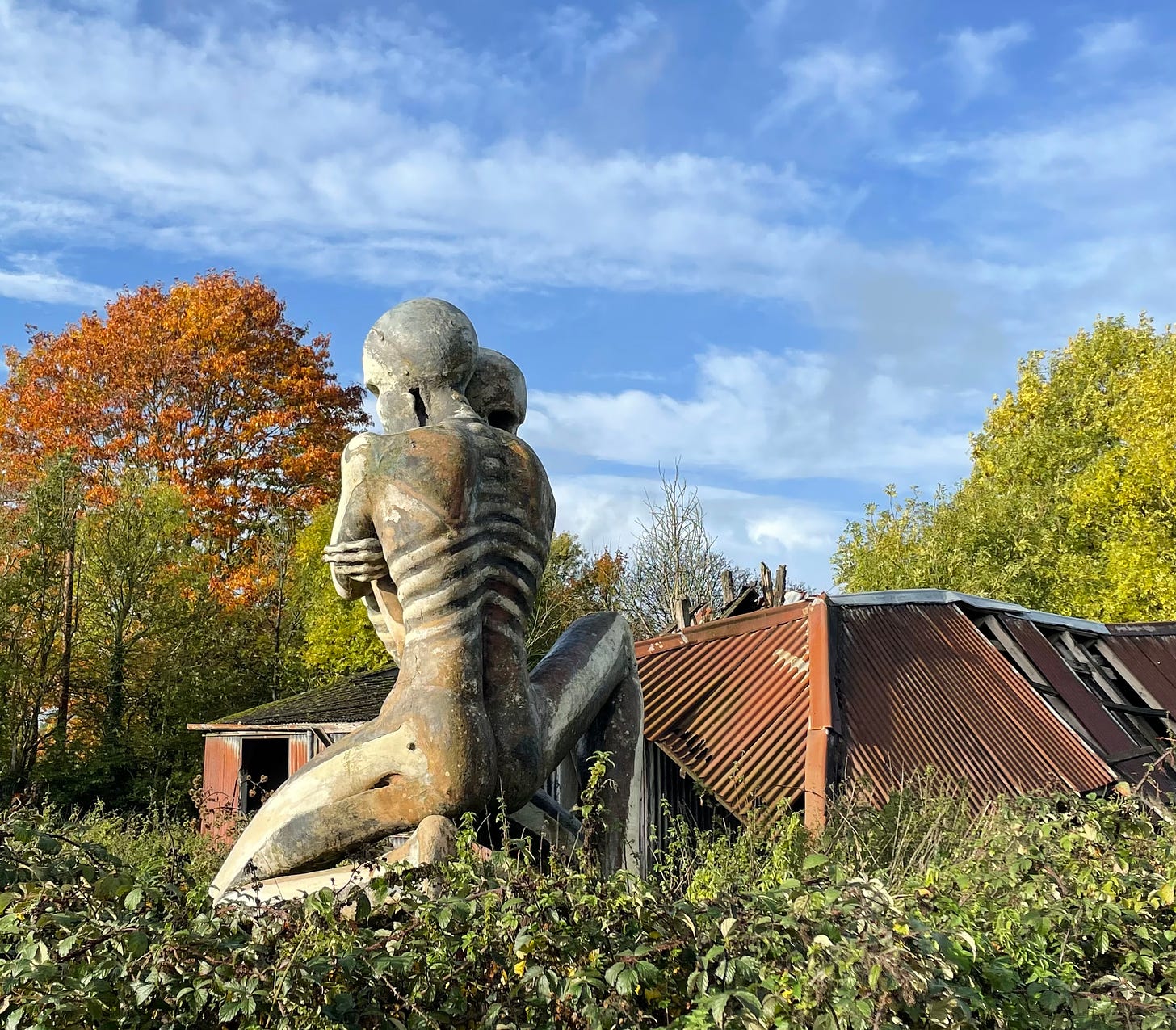 Two embracing fibreglass figures beside run down farm buildings with autumn colours setting